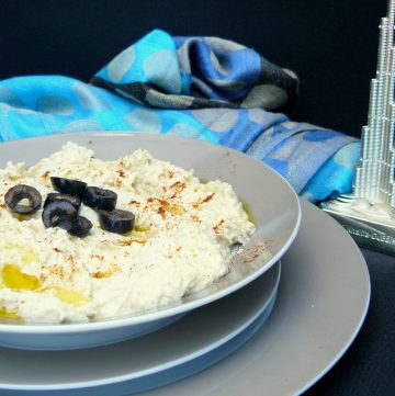 Hummus in a grey bowl garnished with olive oil and black olives