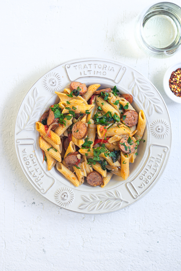 Penne pasta with sausages and tomatoes in white bowl