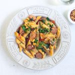 Penne pasta with sausages and tomatoes in white bowl
