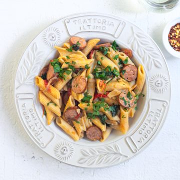 Penne pasta with sausages and tomatoes in white bowl