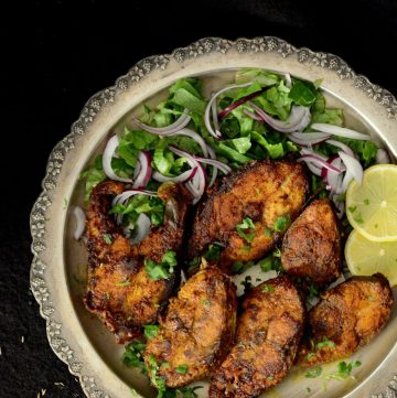 Fish fry slices on a silver platter with greens and lemon wedges