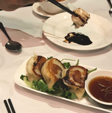 Three pan fried pork and prawn dumplings served on salad leaves in a white platter