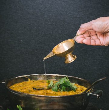 Hand pouring ghee on rice dish in bowl