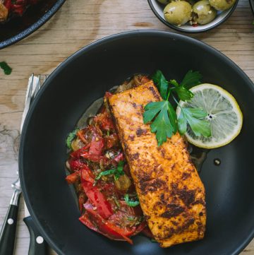 Pan fried salmon with peperonata in black bowl