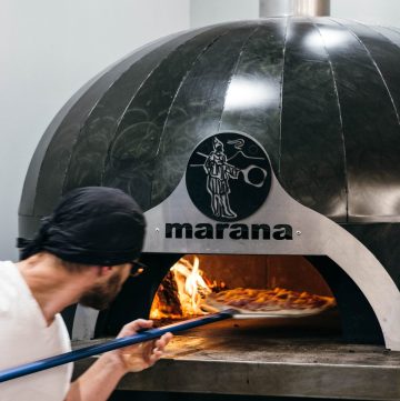 man placing pizza in woodfired oven