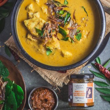 Indian style fish curry in black bowl with a bottle of seafood curry paste on the side