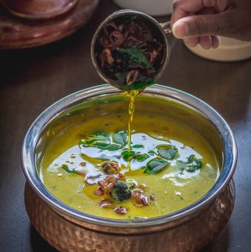 Hand pouring ghee into a bowl of Kerala lentil curry