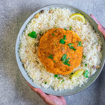 whole roasted tandoori cauliflower on a bed of rice in a blue platter